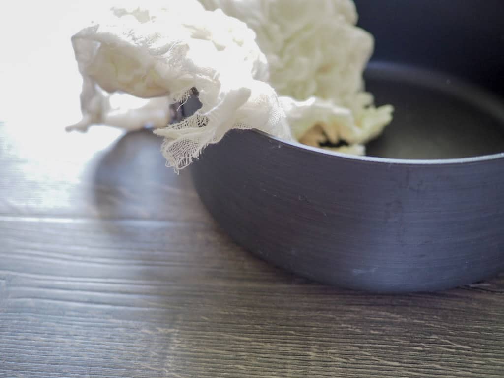 A large shallow saucepan on a gray wooden surface, draped with cheesecloth.