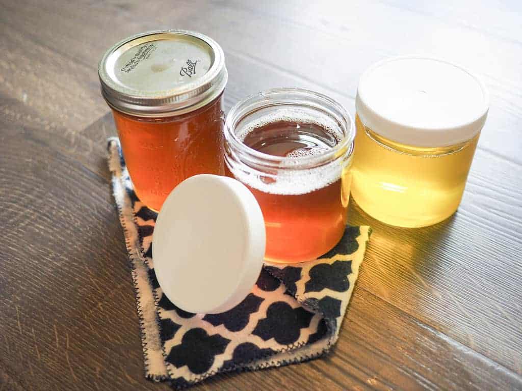 Three glass jars full of homemade clarified butter, one lid is open.