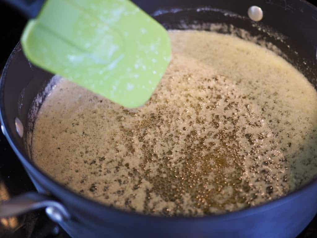 A large black saucepan filled with golden melted butter and a green rubber spatula.