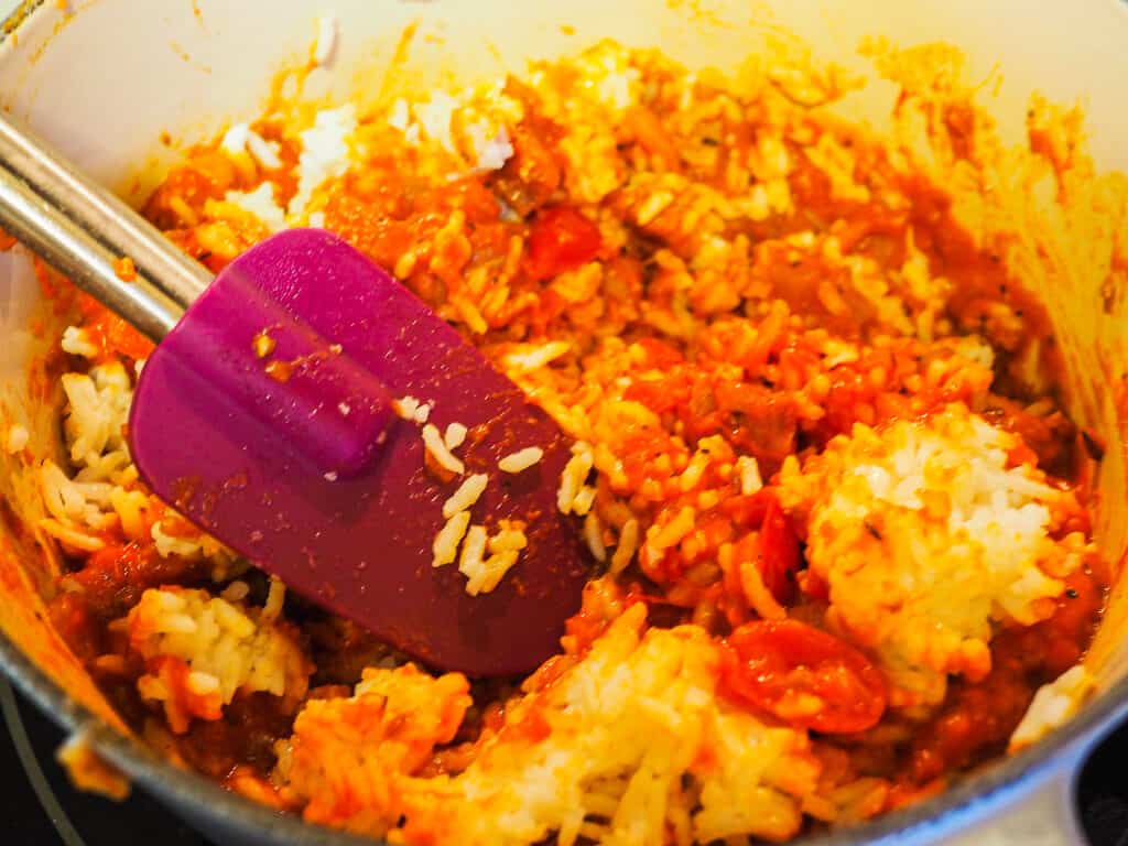 A pot of rice with tomato sauce and a purple spatula.