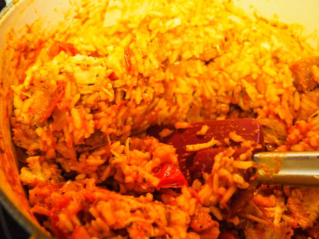 A pot of rice with tomato sauce and a purple spatula.
