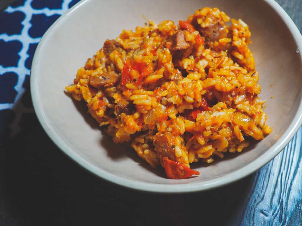 A bowl of rice with chicken and sausage with a blue and white napkin.