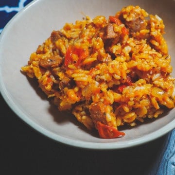 A bowl of creole tomato rice with chicken and sausage with a blue and white napkin.