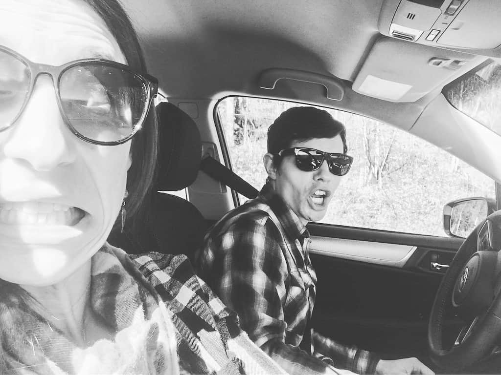 A man and a woman in a car wearing flannel and sunglasses in black and white.