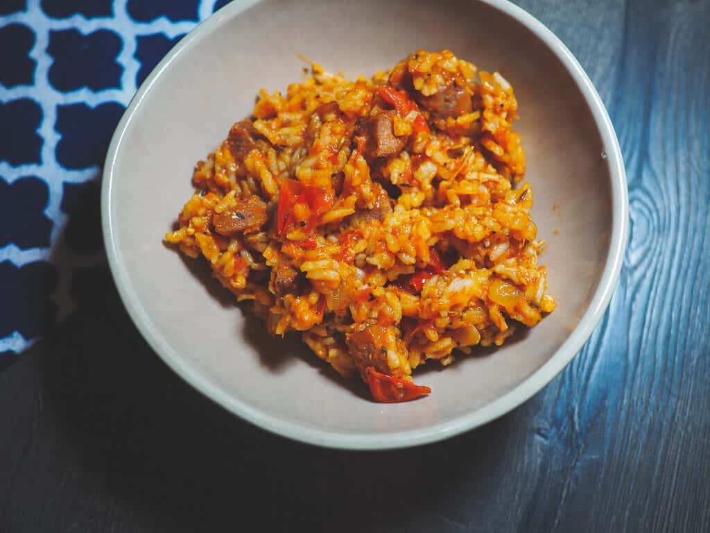 A bowl of rice with chicken and sausage with a blue and white napkin.