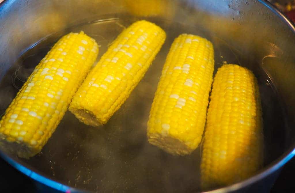 Four ears of corn boiling in a pot of water.