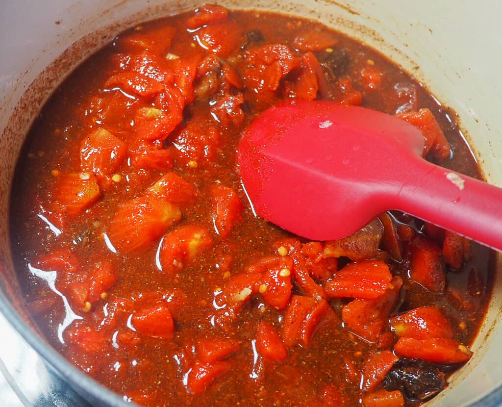 A white pot with tomatoes and a sauce simmering to make barbecue sauce.