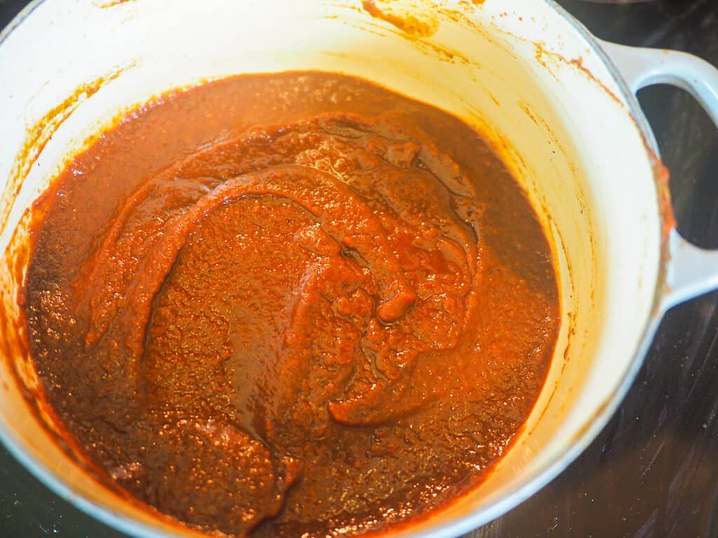 A white pot with reddish brown barbecue sauce simmering in it.
