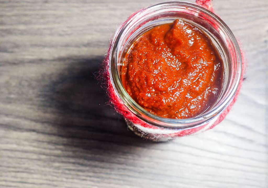 A jar of barbecue sauce with a ribbon around the top on a gray wooden background.
