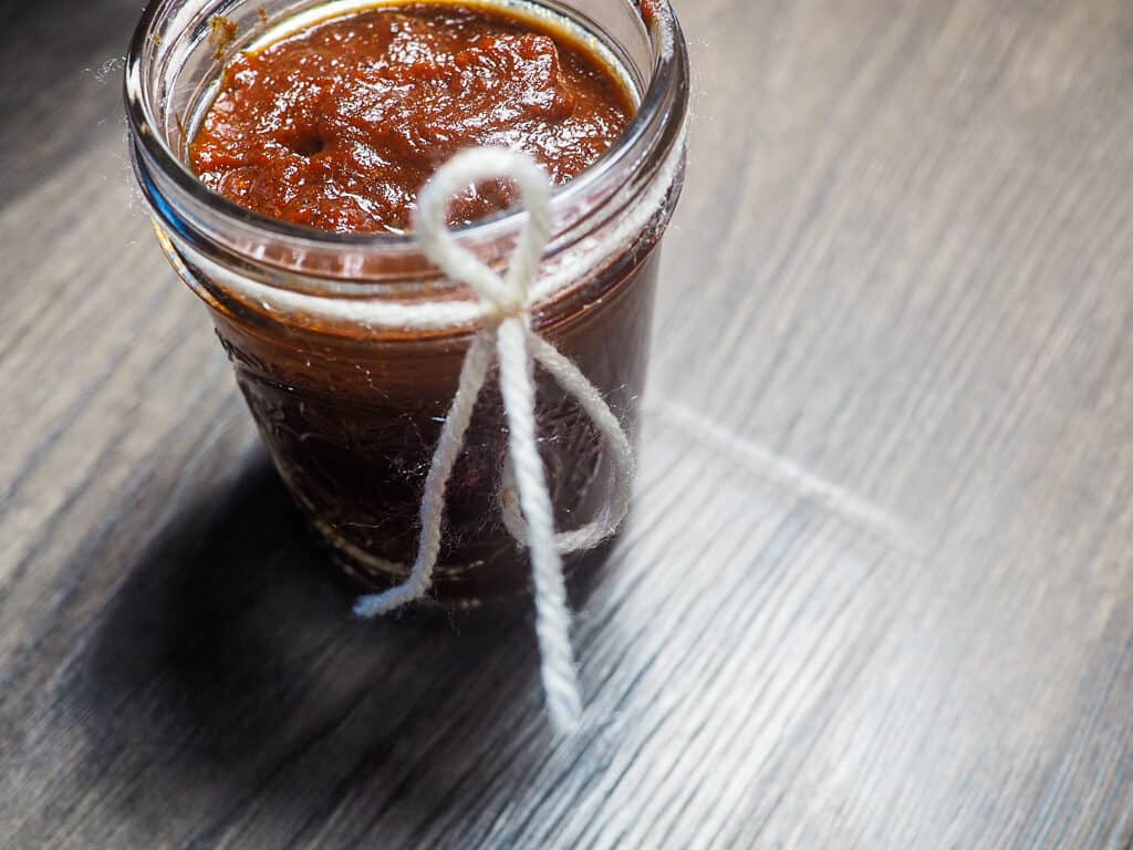 A jar of barbecue sauce with a ribbon around the top on a gray wooden background.