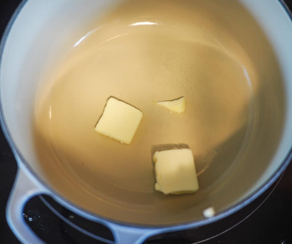 Squares of butter melting in a small, white and gray pot.