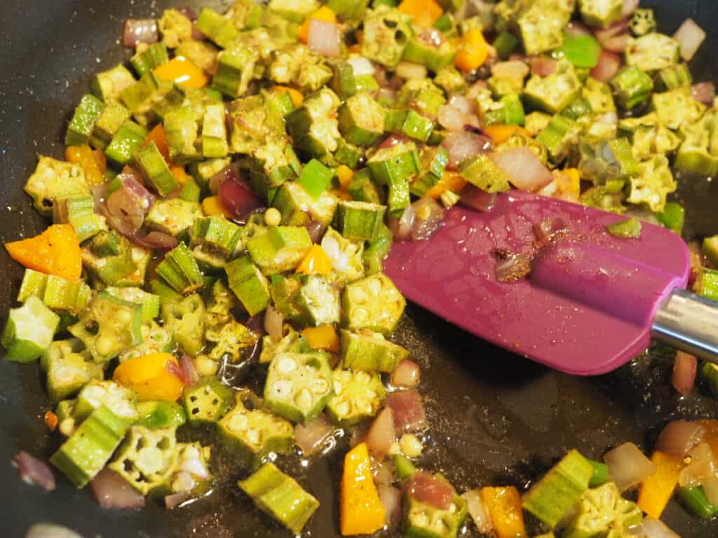 A saute pan with cooked okra and a purple spatula.