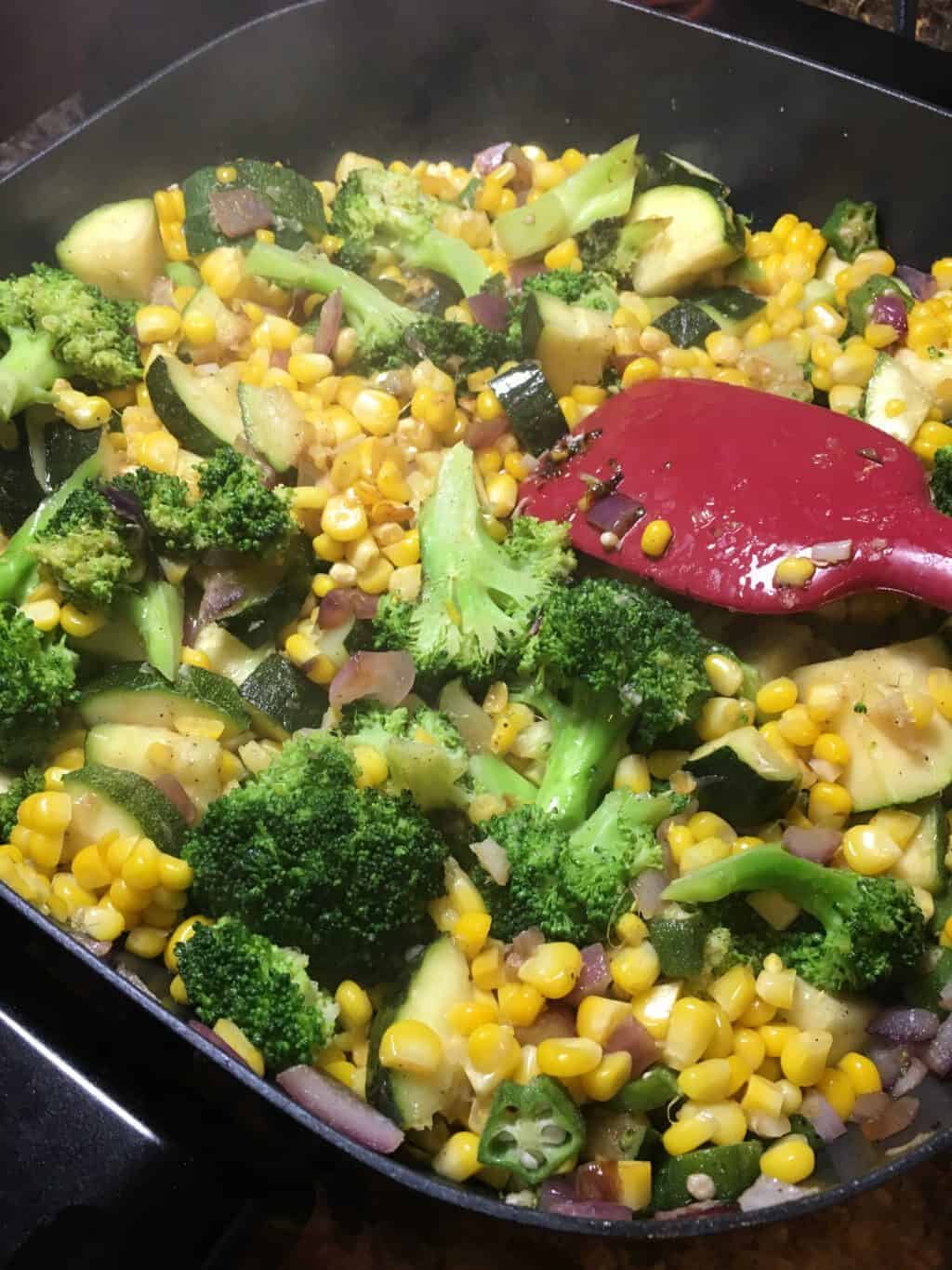 Corn, brocolli, zucchini, and red onions in a skillet.