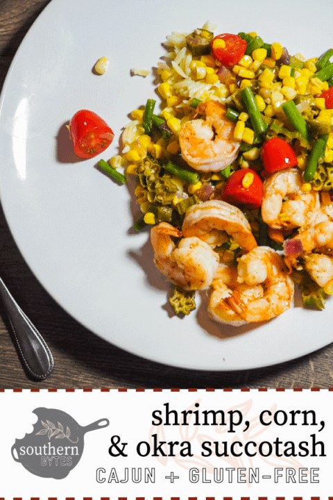 A white dish with shrimp, tomatoes, corn, and okra and a red and white dishtowel with a fork on a gray background.