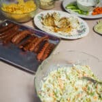 A kitchen counter with hot dogs, coleslaw, a bloomin onion, and dishes of vegetables.