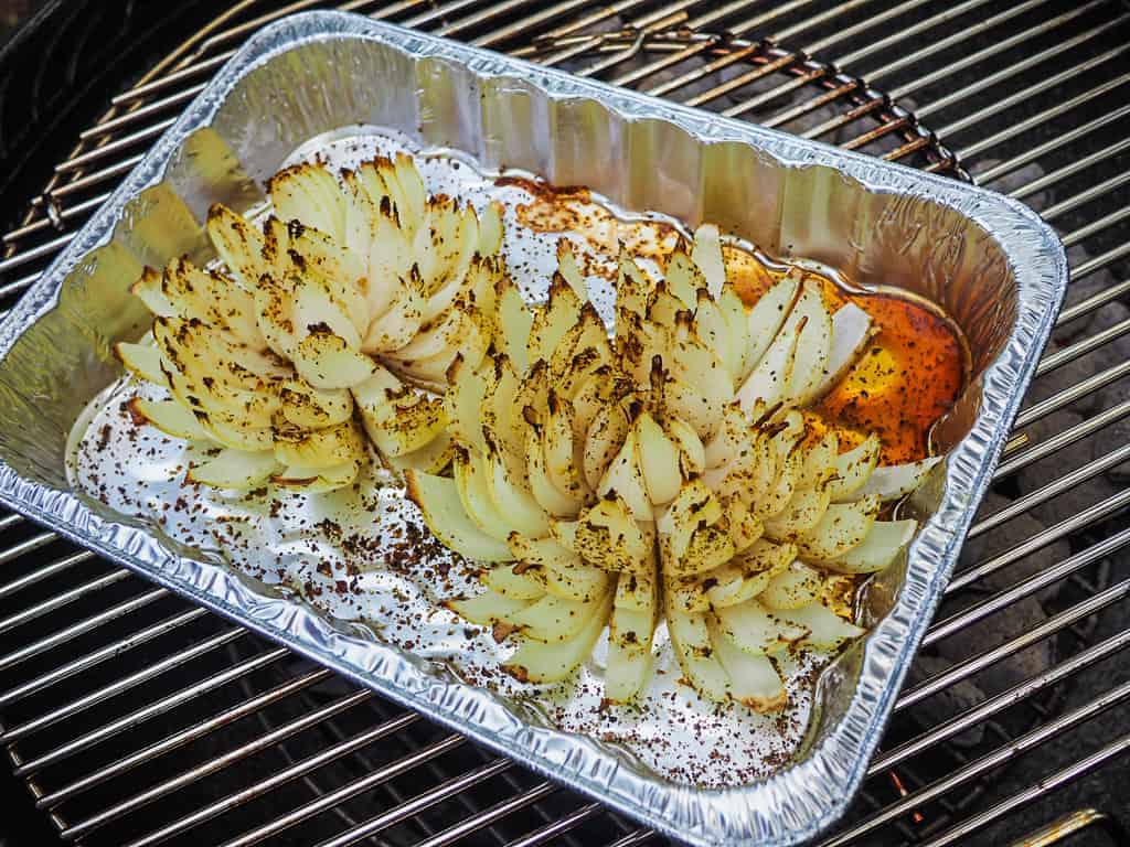A bloomin onion in an aluminum pan on a grill.