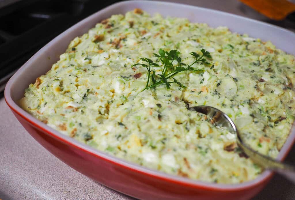 A large red and white bowl with egg and potato salad.