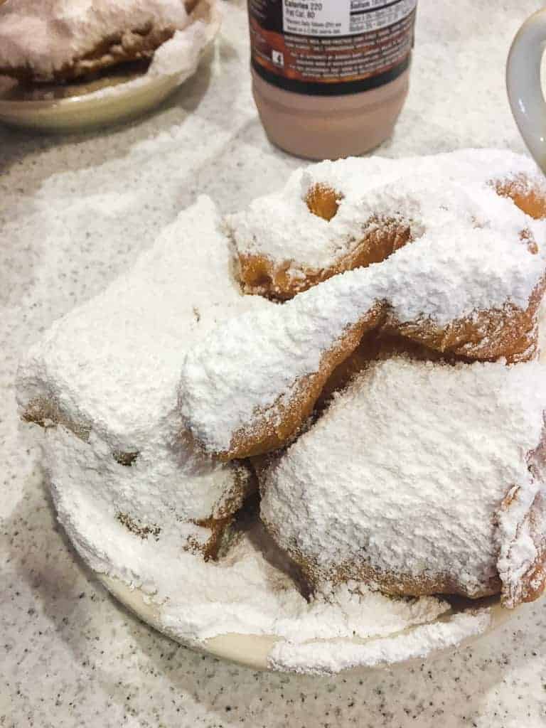 A plate of beignets covered in powdered sugar with a chocolate milk from Cafe du Monde in New Orleans.