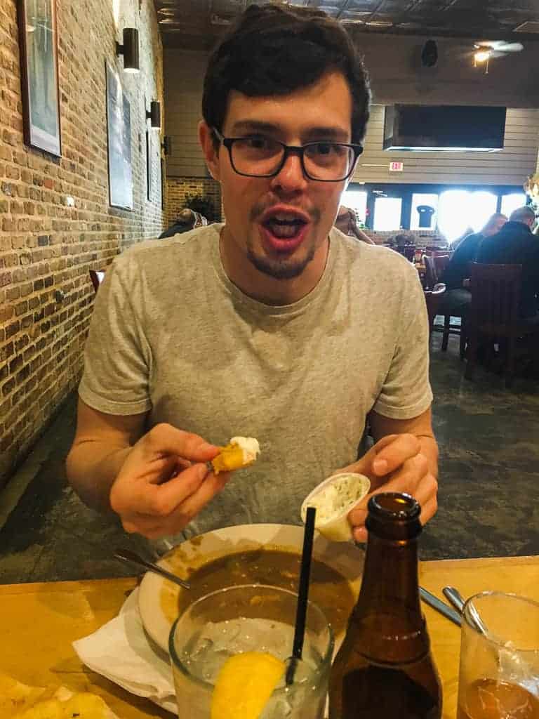 A man with dark hair and glasses eating friend seafood and gumbo and looking very excited about it.