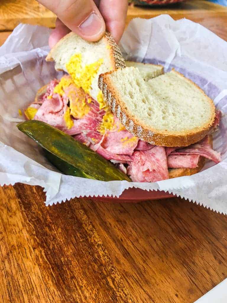 A mortadella and mustard sandwich in a basket with a pickle from Stein's Deli in New Orleans.