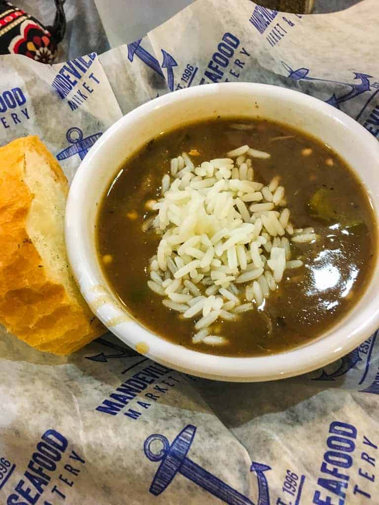A white bowl filled with seafood gumbo and a slice of french bread.