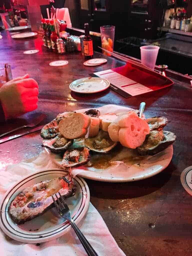 A plate of chargrilled oysters on a bar top in a dark room.