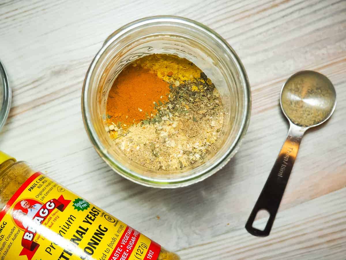 A mason jar full of spices used to make homemade paleo chicken bouillon. Thyme, nutritional yeast, salt, ginger, umami, and oregano.