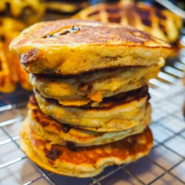 A stack of paleo sweet potato chocolate chip pancakes and waffles on a cooling rack.