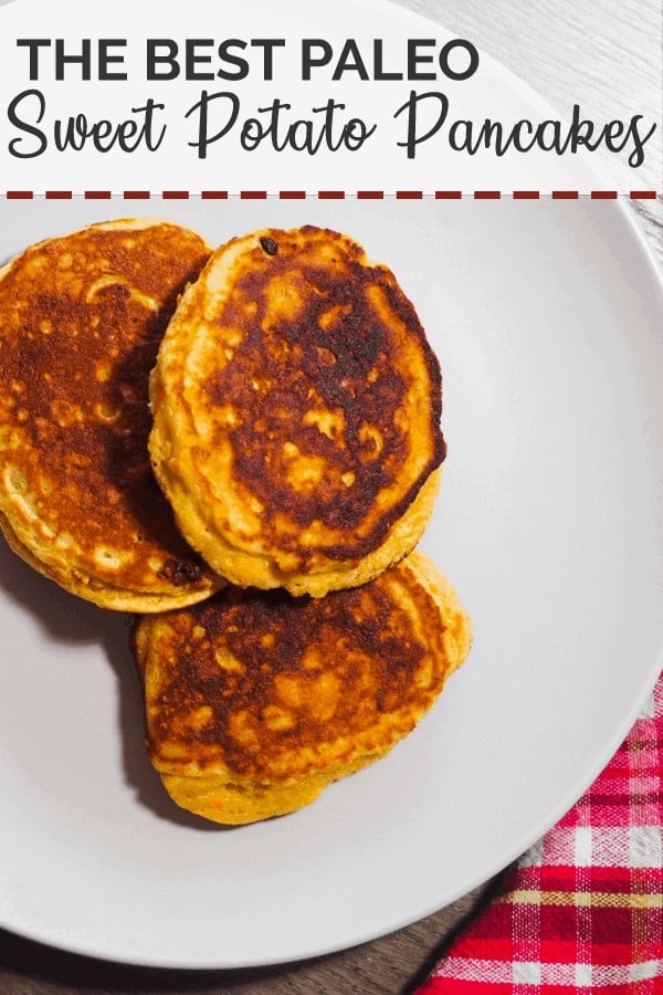 Three sweet potato paleo pancakes on a white plate with a red checkered napkin and small bottle of maple syrup.