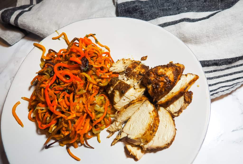 A zoomed out white plate with crispy sweet potato noodles and sliced Jamaican Jerk Chicken with a gray and navy dish towel.