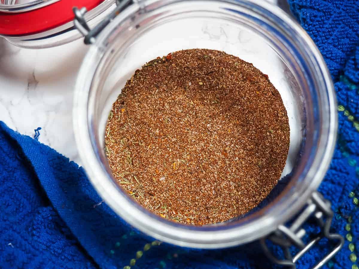 A small jar with the mixed ingredients of Jamaican Jerk Seasoning and a blue dish cloth.