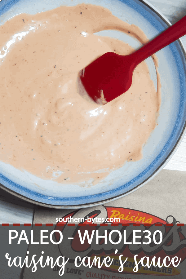 A pin image of a blue and white bowl of orange Raising Cane's dipping sauce with a red spatula and a Cane's napkin.