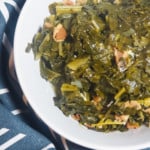 A white bowl of paleo collard greens with bits of bacon on a blue and white towel.