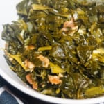 A white bowl of paleo collard greens with bits of bacon on a blue and white towel.