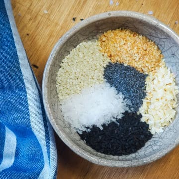 A a bowl of the unmixed ingredients in everything bagel seasoning and a blue dish towel.