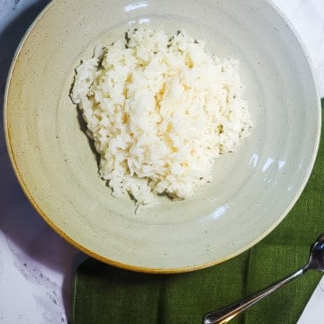 A bowl of white rice on a marble background with a green napkin and a spoon.