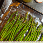 A pin image of a sheet pan covered in foil with oven roasted asparagus and a jar of ghee.