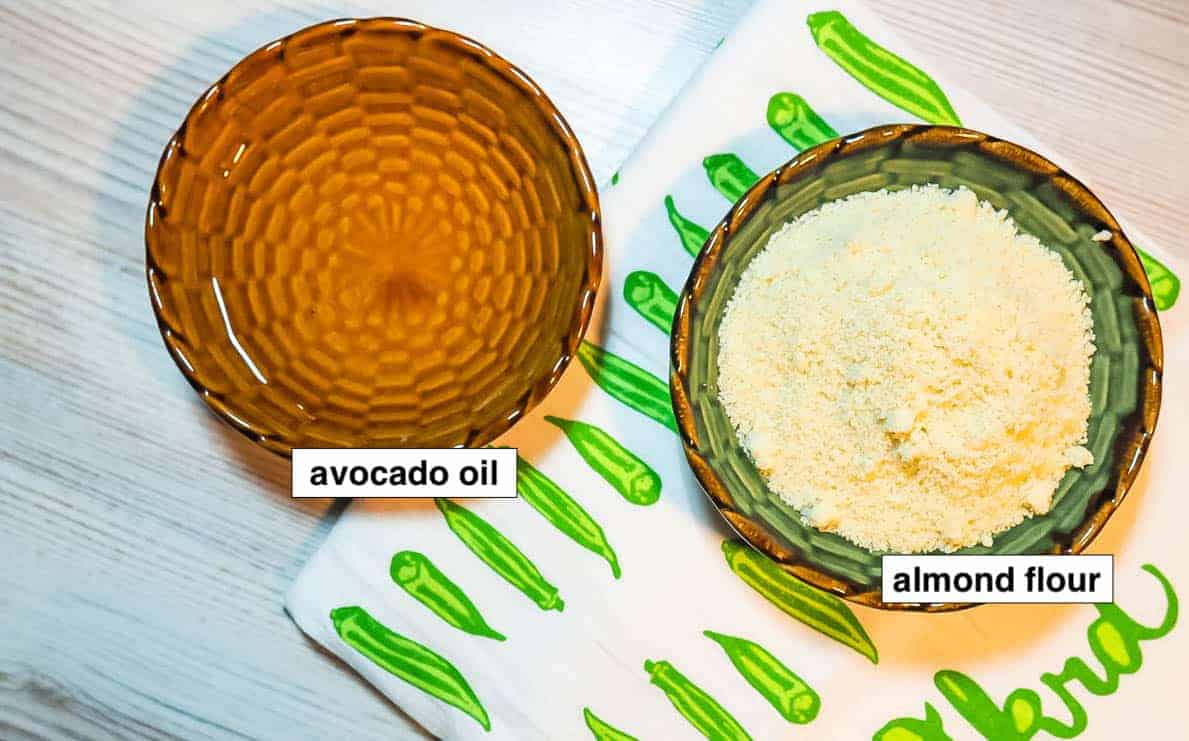 Two small green bowls on an okra tea towel. One is almond flour and one is avocado oil.