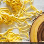 A pin image of piles of homemade paleo pasta on a white wooden board.