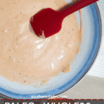 A pin image of a blue and white bowl of orange Raising Cane's dipping sauce with a red spatula and a Cane's napkin.