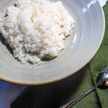 A zoomed in image of a bowl of white rice on a marble background with a green napkin and a spoon.