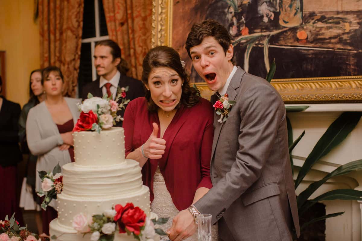 A newly married couple making stupid faces while cutting their wedding cake.