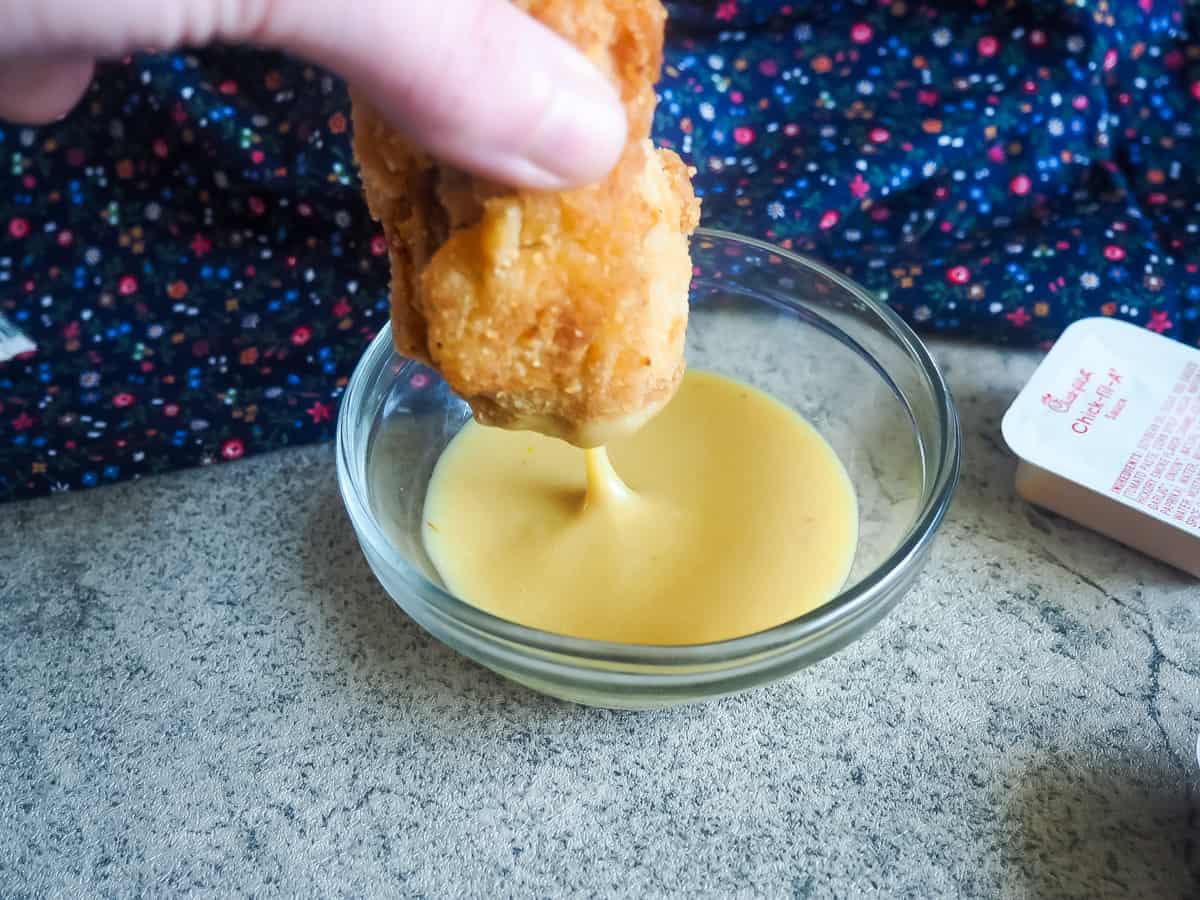A chicken nugget being dunked into a small glass bowl of copycat chick-fil-a sauce.