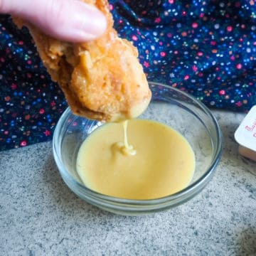 A chicken nugget being dunked into a small glass bowl of copycat chick-fil-a sauce.