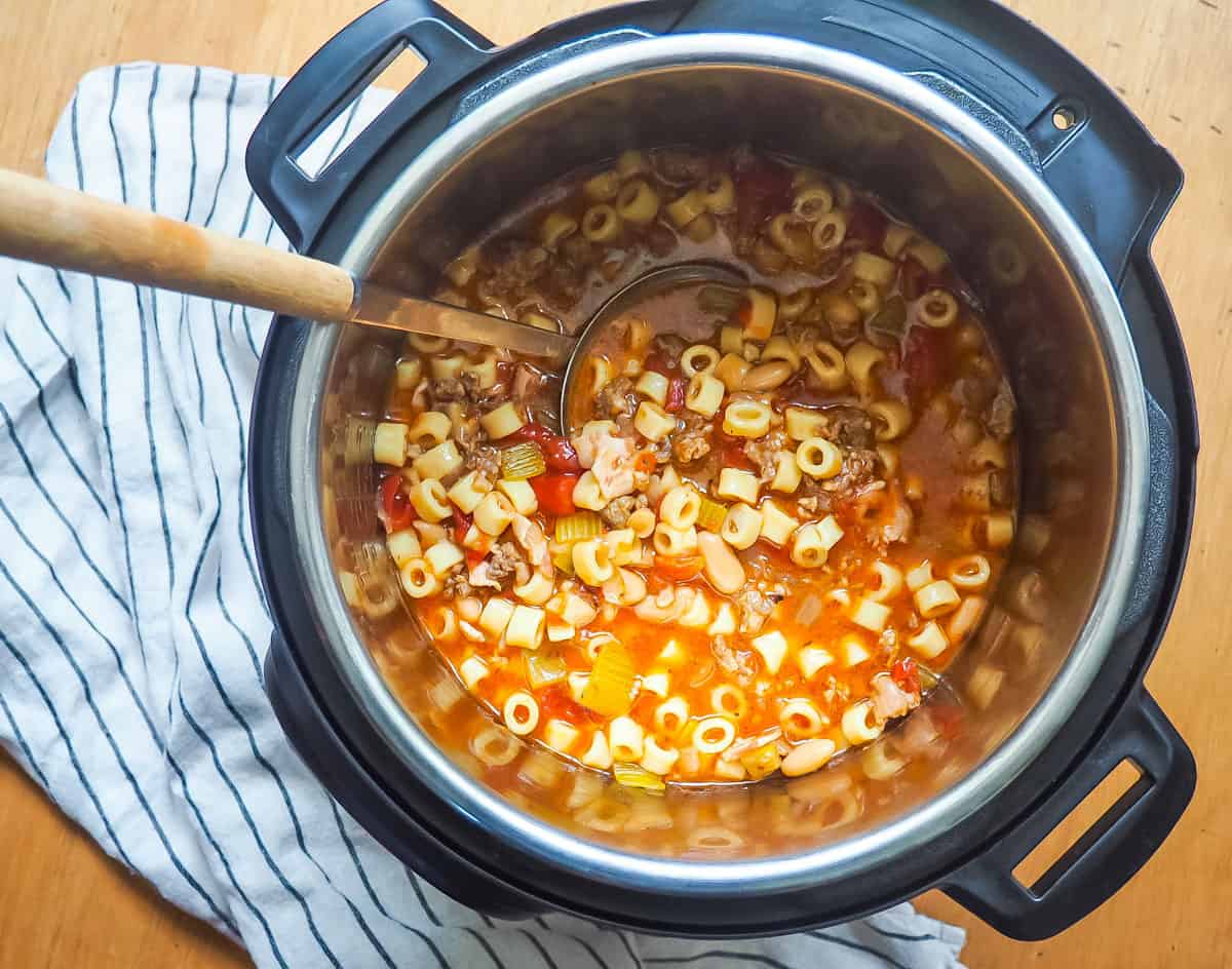 A instant pot of pasta e fagioli with a ladle scooping some out.