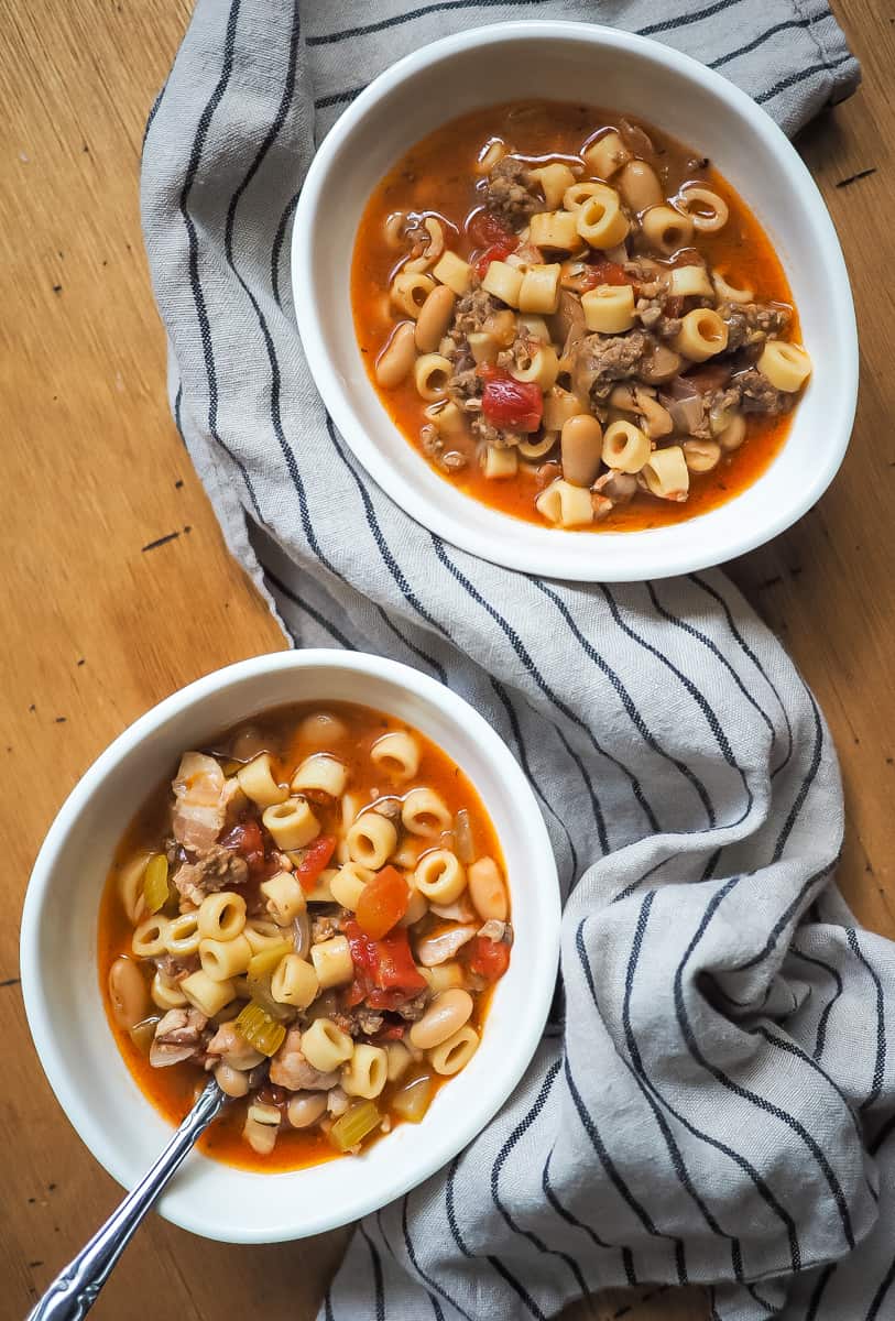 Two white bowls of pasta e fagioli on wooden background.