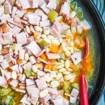 A crockpot filled with white beans and ham, cooking.
