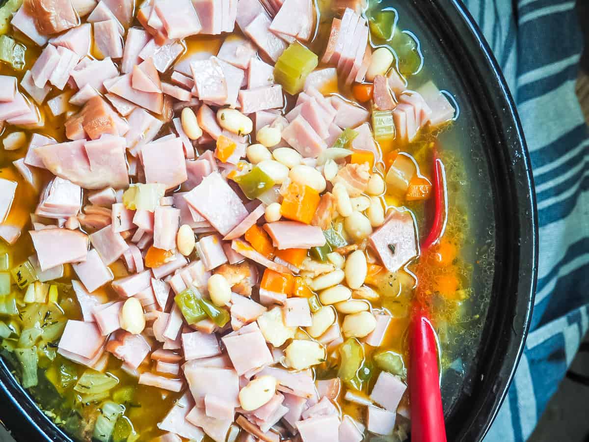 A crockpot filled with white beans and ham, cooking.