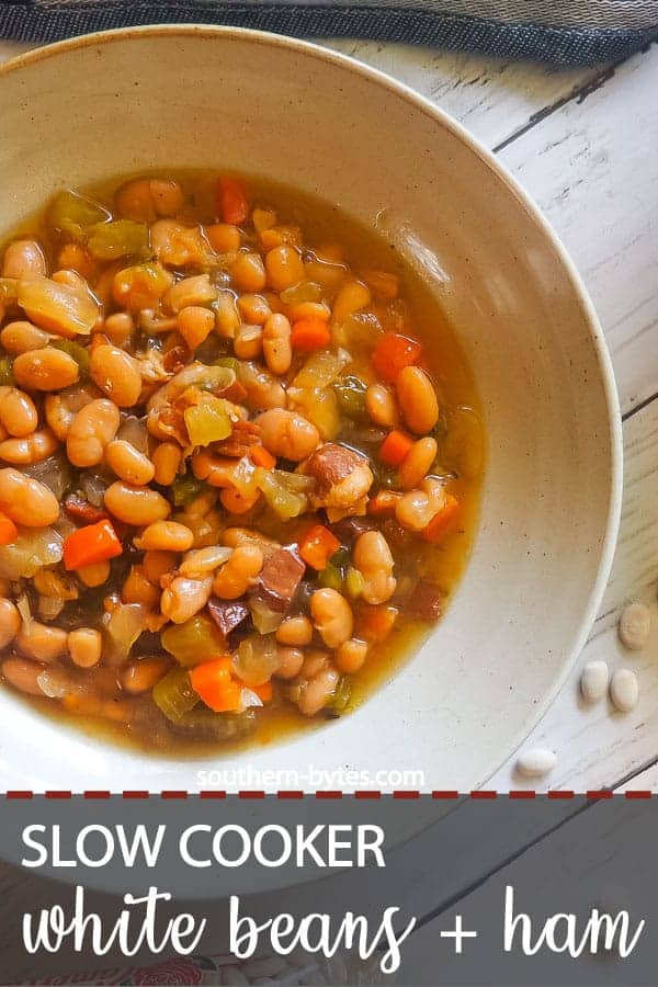 A pin image of a bowl of white beans and ham with Camellia beans spread around it.