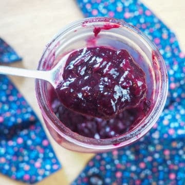 A spoon of paleo blueberry jam in a large jar.